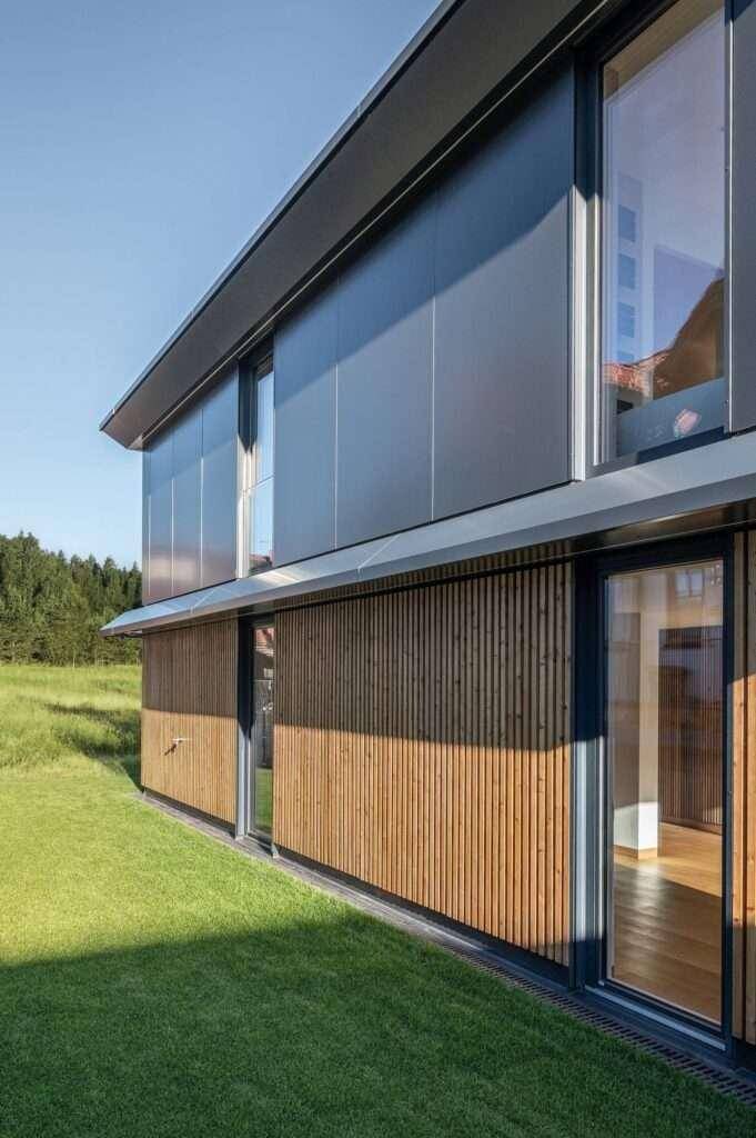 Seitenansicht eines modernen Hauses mit Holzverkleidung, großen Fenstern und angrenzendem Rasen.