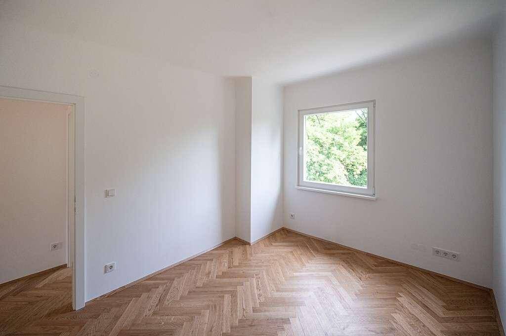Unmöbliertes Zimmer mit Fischgrätparkett und einem Fenster, das viel Tageslicht bietet.