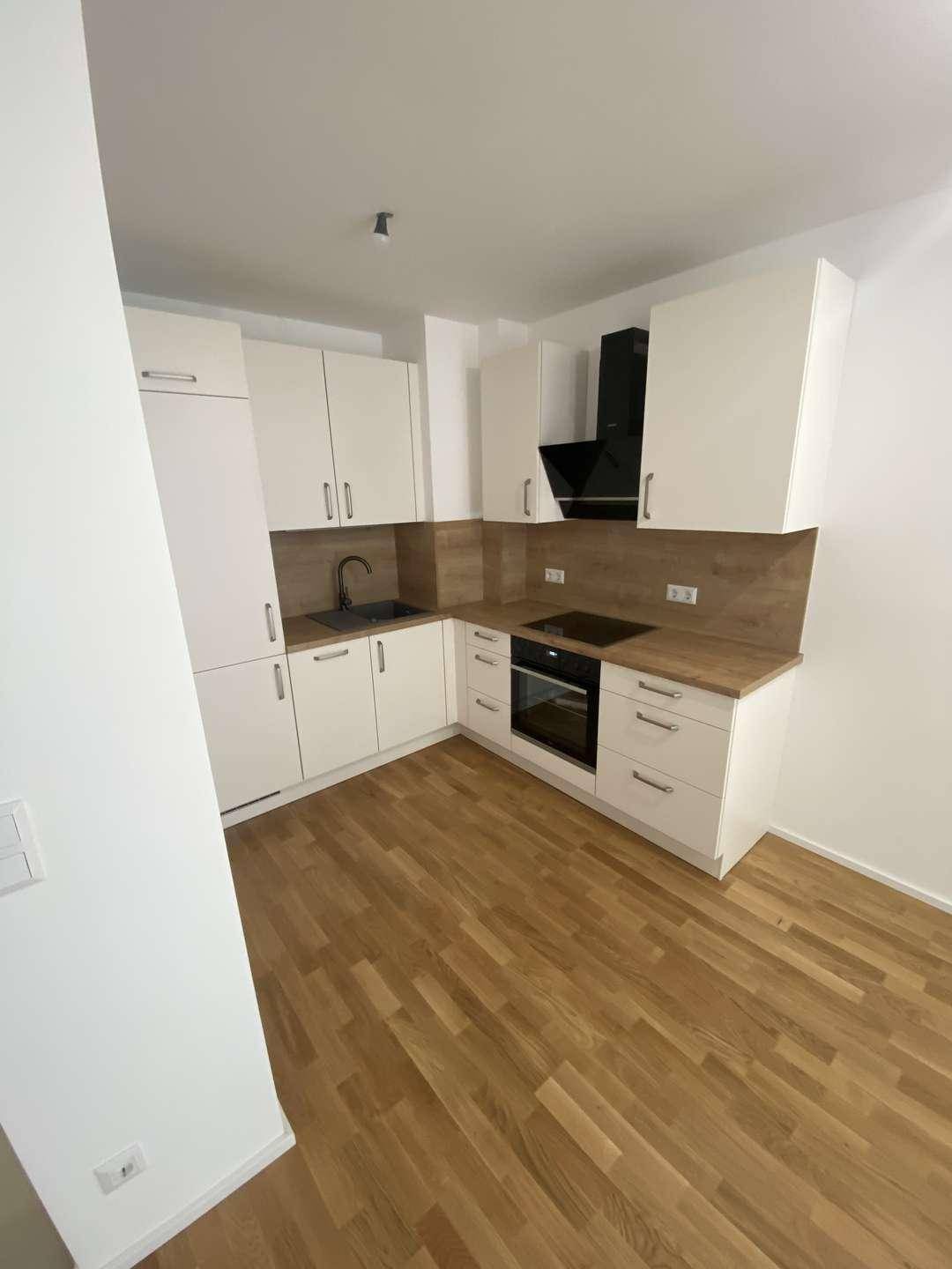 Neue Küche mit weißen Fronten, Holzoptik-Arbeitsplatte und modernen Geräten in einem hellen Raum.