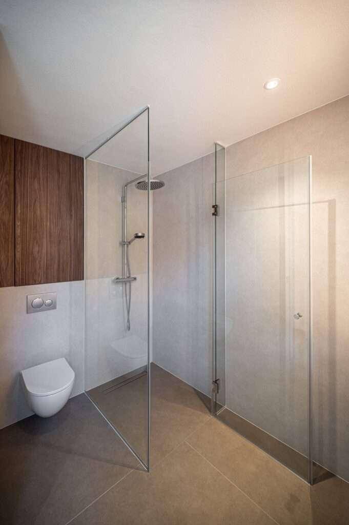 Elegantes Badezimmer mit bodengleicher Dusche, wandhängender Toilette und Holzdetails.