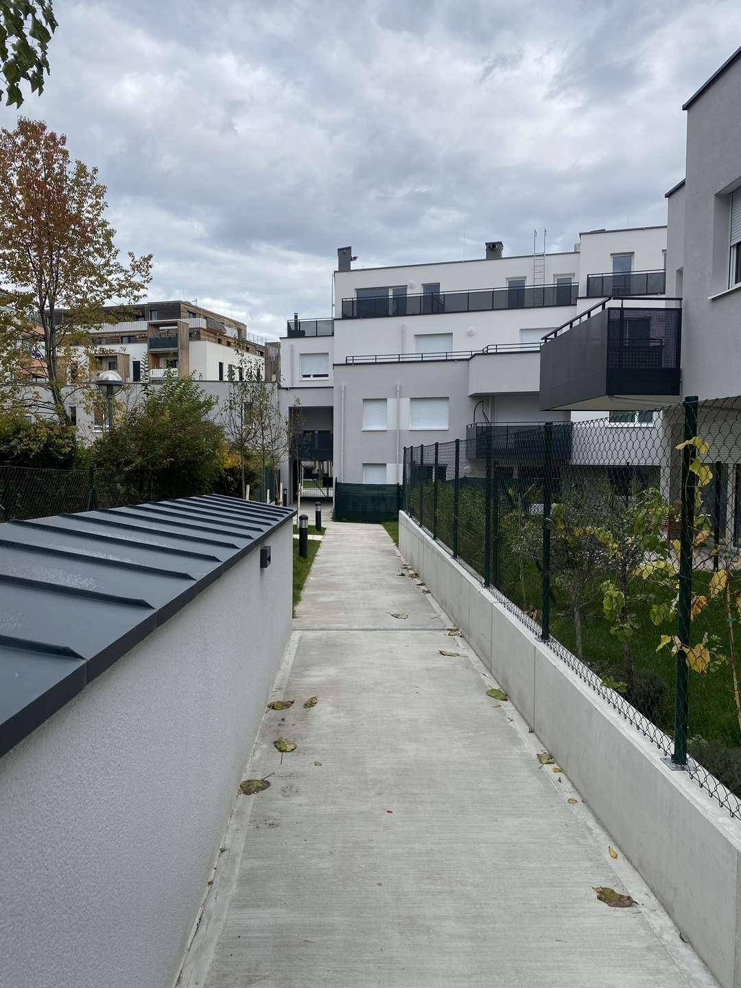 Außenbereich eines modernen Wohnkomplexes mit Gehwegen und begrünten Flächen unter bewölktem Himmel.