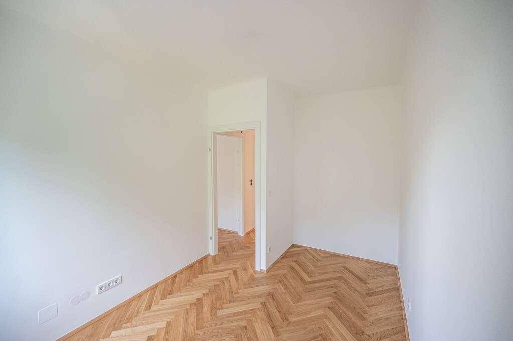 Unmöbliertes Zimmer mit Fischgrätparkett und Zugang zu einem Flur, ideal als Schlafzimmer.