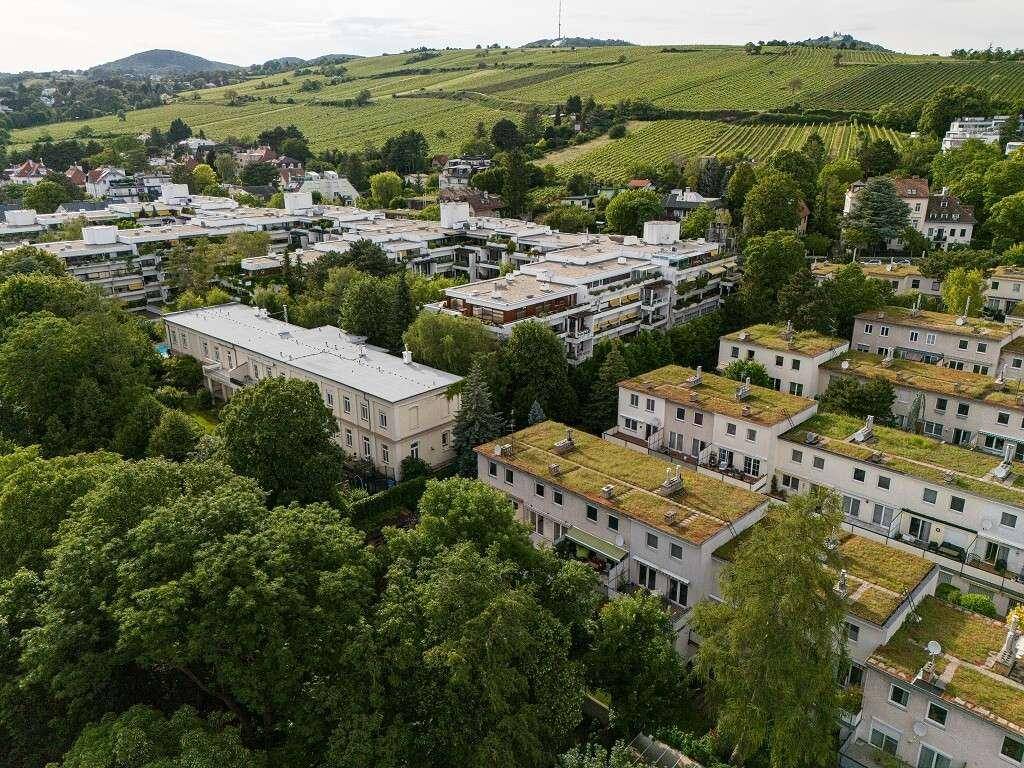 Luftaufnahme einer Wohnsiedlung mit viel Grün, Bäumen und Weinbergen im Hintergrund.
