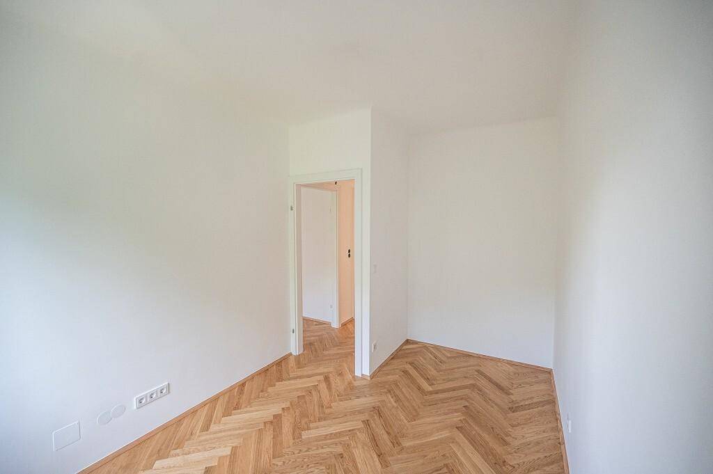 Helles Zimmer mit Fischgrätparkett und Zugang zu einem weiteren Raum, ideal als Schlafzimmer.