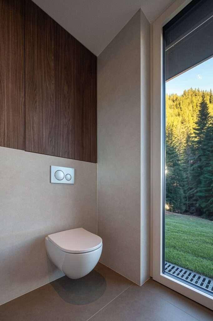 Modernes WC mit Wand-WC, Holzverkleidung und großem Fenster mit Blick ins Grüne.