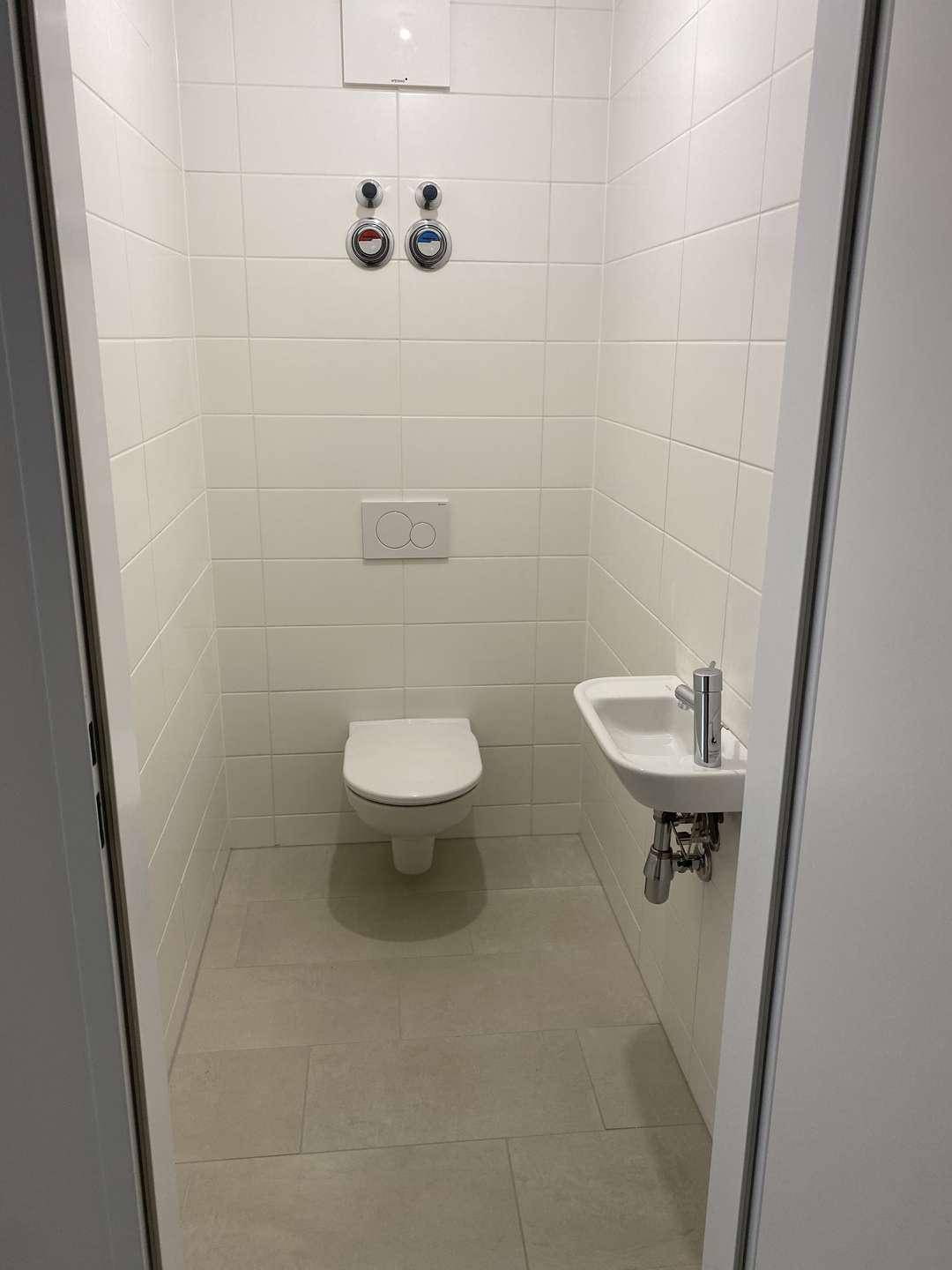 Modernes Gäste-WC mit wandhängender Toilette, kleinem Waschbecken und weißen Fliesen an den Wänden.