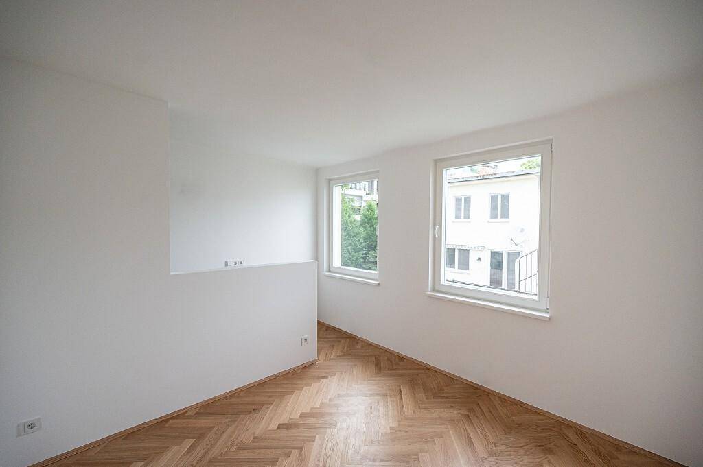 Helles Zimmer mit Fischgrätparkett und zwei Fenstern, die einen angenehmen Blick nach draußen bieten.