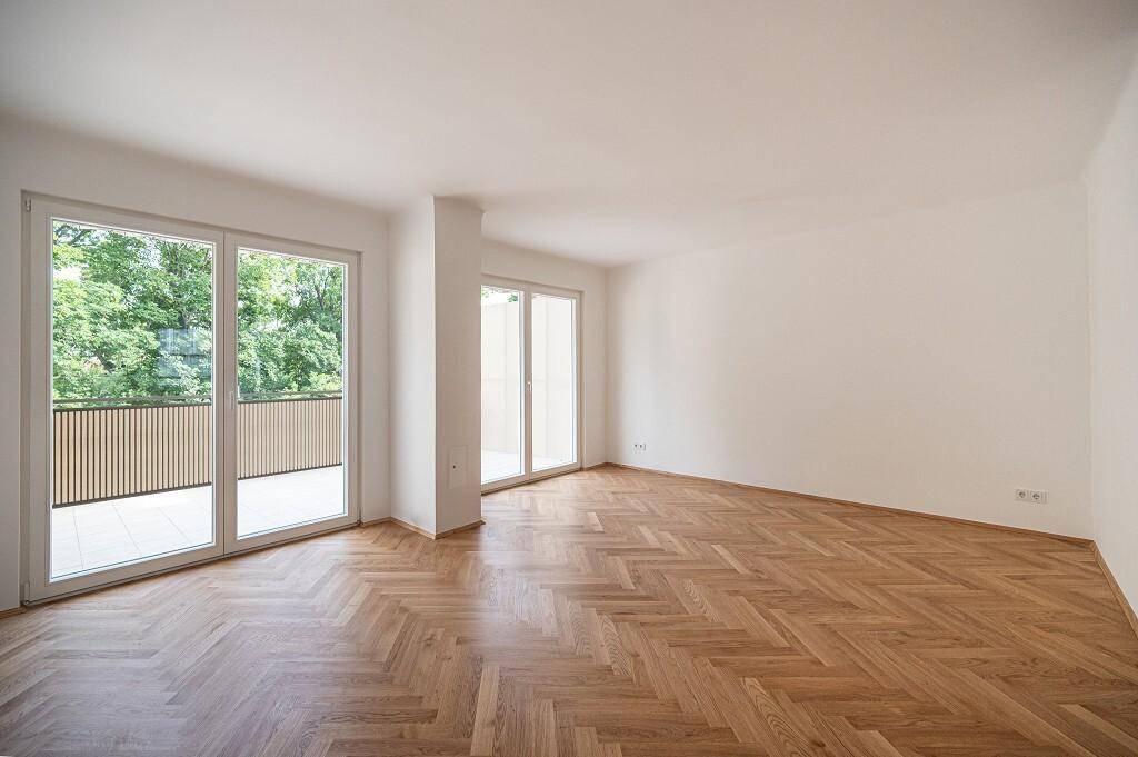 Heller Wohnbereich mit Fischgrätparkett und mehreren Fenstertüren, die viel Tageslicht hereinlassen.