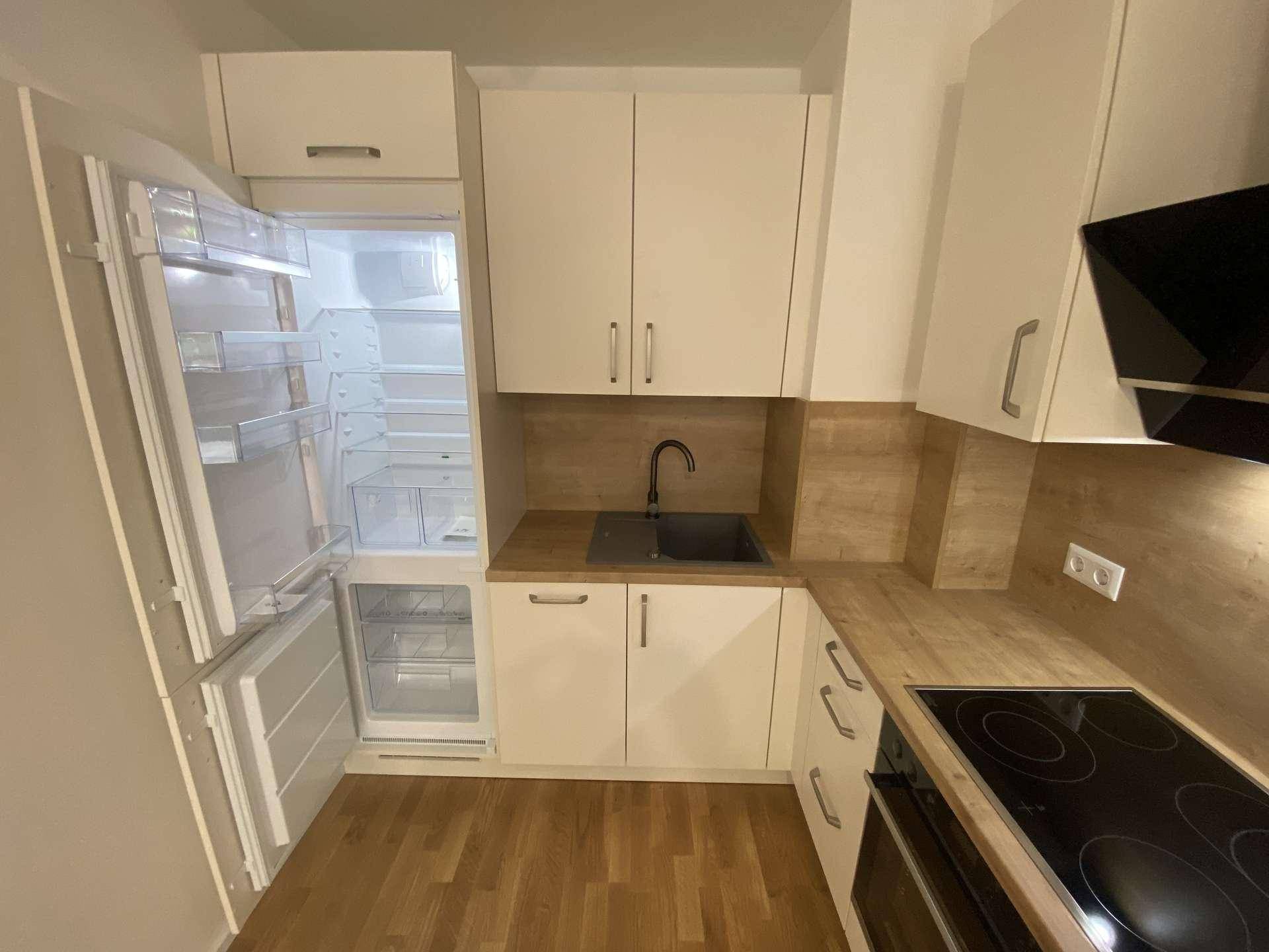 Moderne Einbauküche mit weißen Schränken, Holzoptik-Arbeitsplatte und integriertem Kühlschrank mit Gefrierfach.