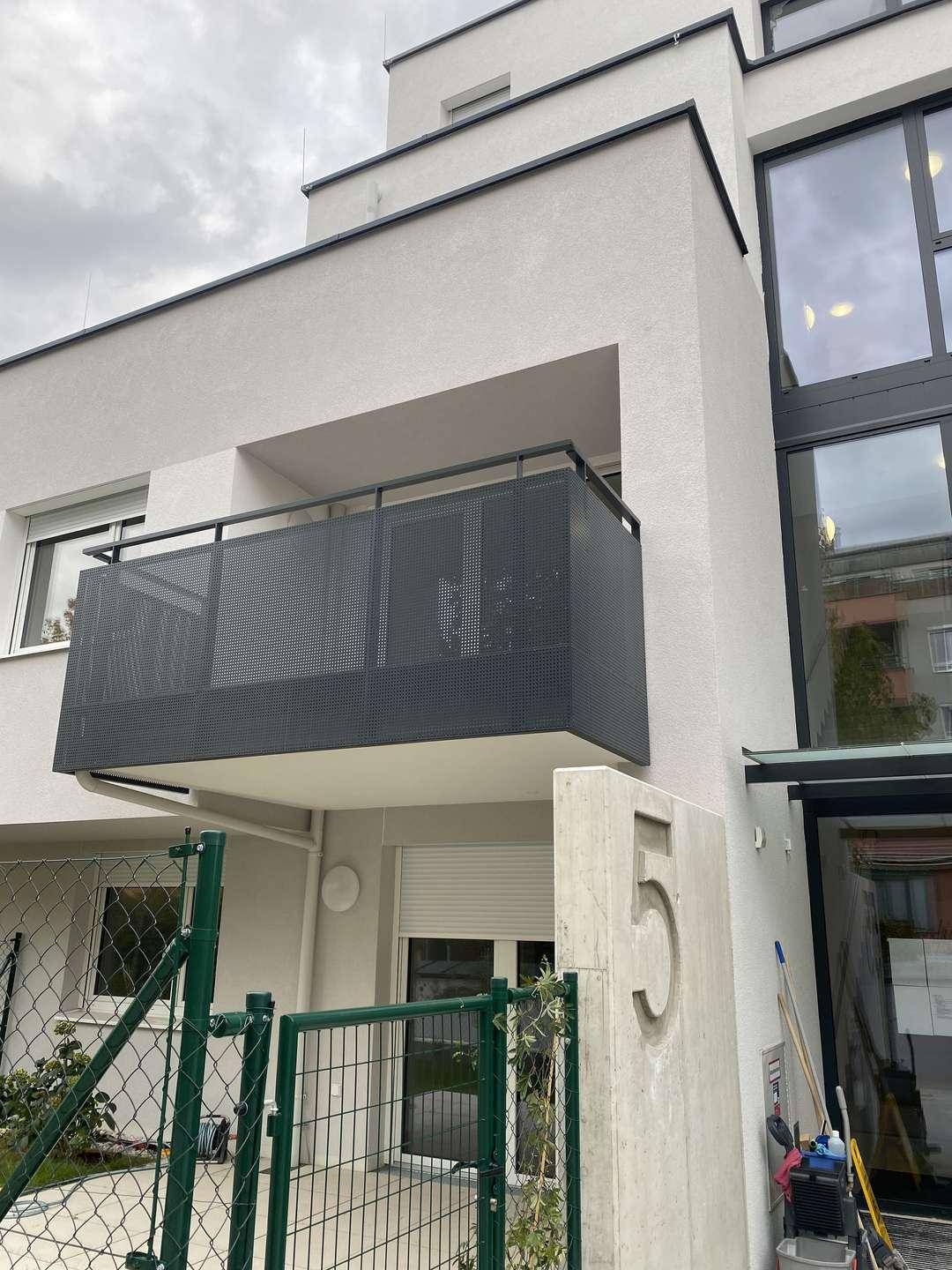 Moderner Balkon mit dunklem Gittergeländer an der Fassade eines Neubaus mit schlichtem Design.