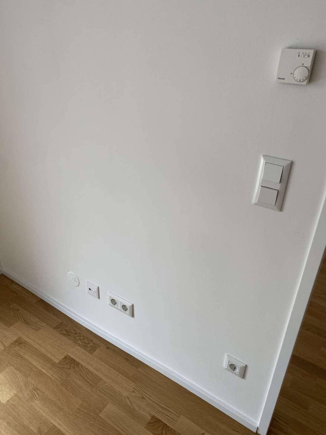 Wandthermostat und elektrische Anschlüsse an einer weißen Wand in einem modernen Raum.