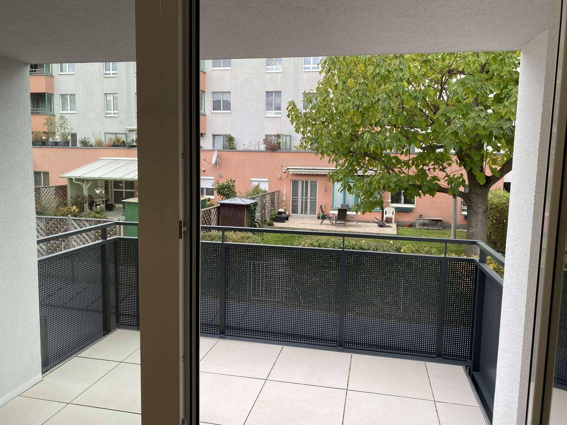 Geräumiger Balkon mit Fliesenboden und Blick auf den begrünten Innenhof und Nachbargebäude.