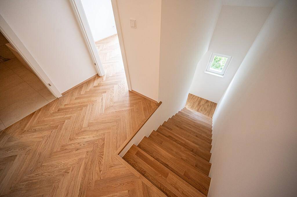 Treppenhaus mit Holzstufen und Fischgrätparkett im Flurbereich, hell und modern gestaltet.