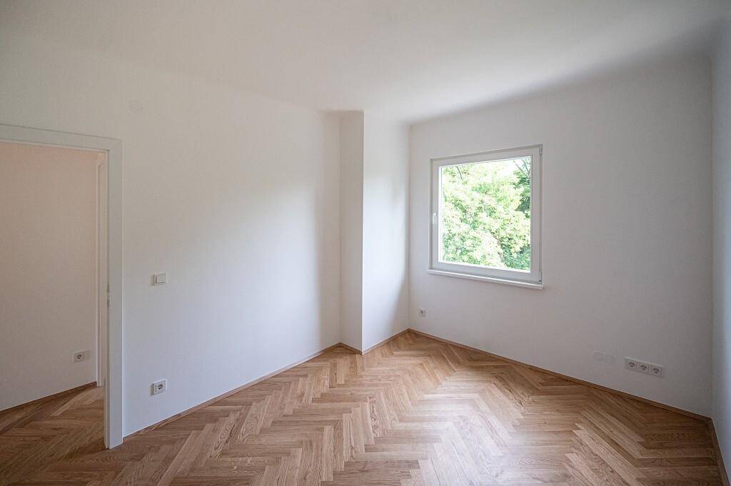 Geräumiges Schlafzimmer mit Fischgrätparkett und einem Fenster, das viel Tageslicht hereinlässt.
