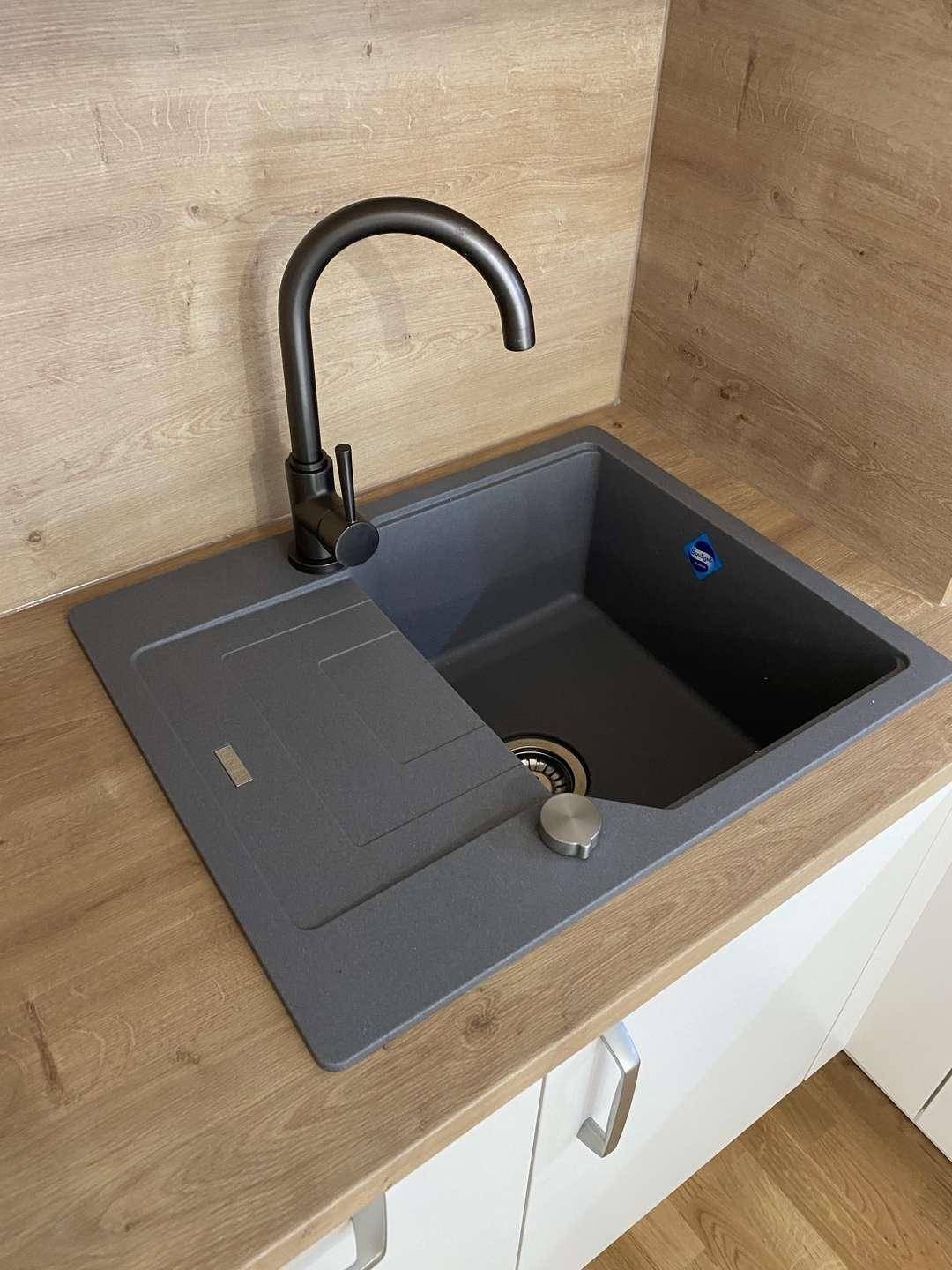 Moderne Küchenspüle aus Granit mit schwarzem Wasserhahn und Holzoptik-Arbeitsplatte in der Küche.