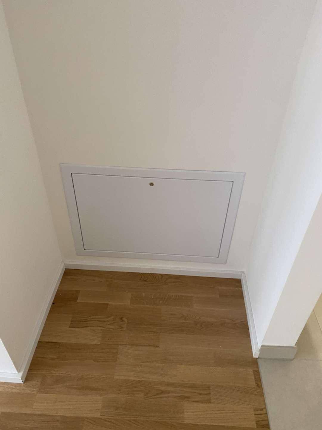Eine weiße Wartungsklappe oder ein Zugang zu einem Installationsschacht in einem Flur oder Abstellraum.