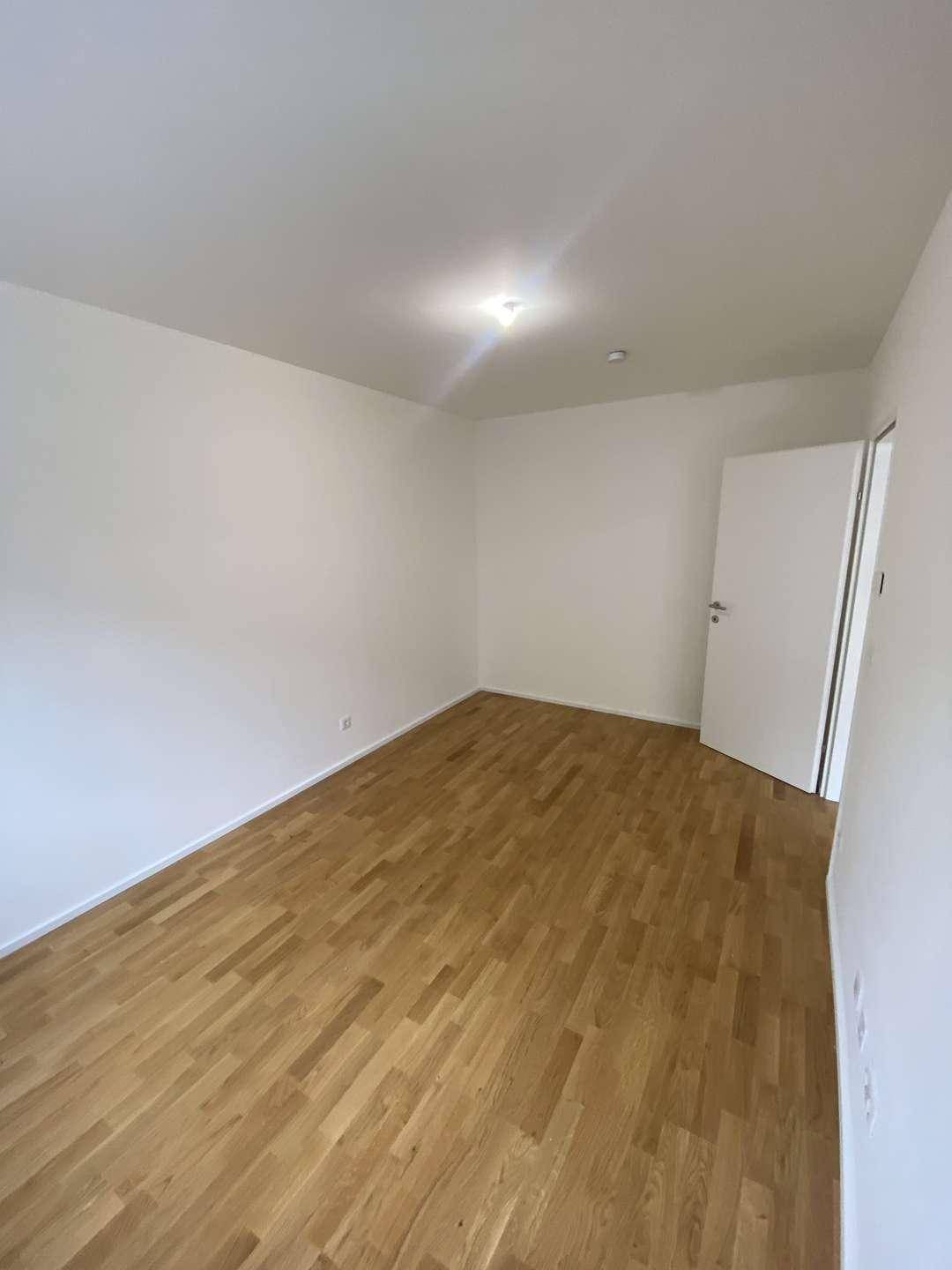 Geräumiges und helles Schlafzimmer mit Parkettboden und weiß gestrichenen Wänden, unmöbliert.