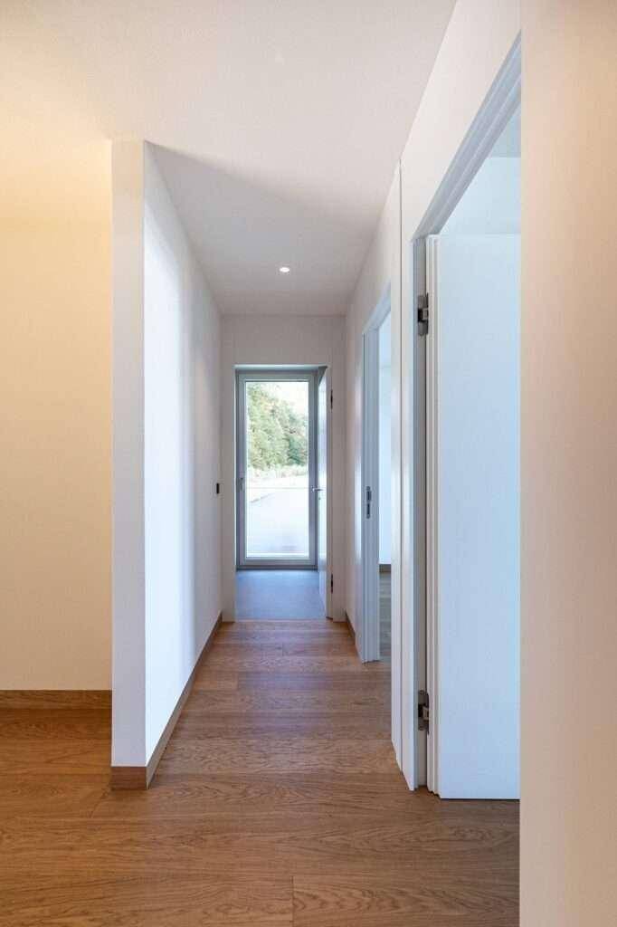 Langer, heller Flur mit Holzboden und Blick auf die Natur durch ein Fenster am Ende.