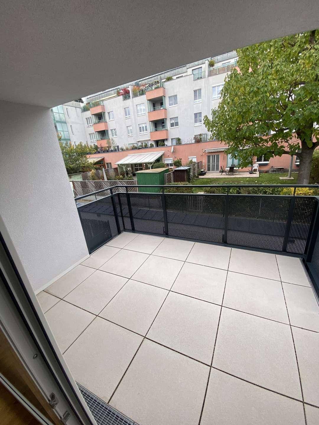 Moderner Balkon mit Fliesenboden und schwarzem Gittergeländer, bietet einen ruhigen Blick auf den Innenhof.