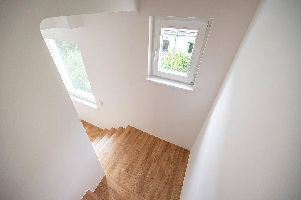 Treppenhaus mit Holzstufen und einem Fenster, das Tageslicht in den Flur bringt.