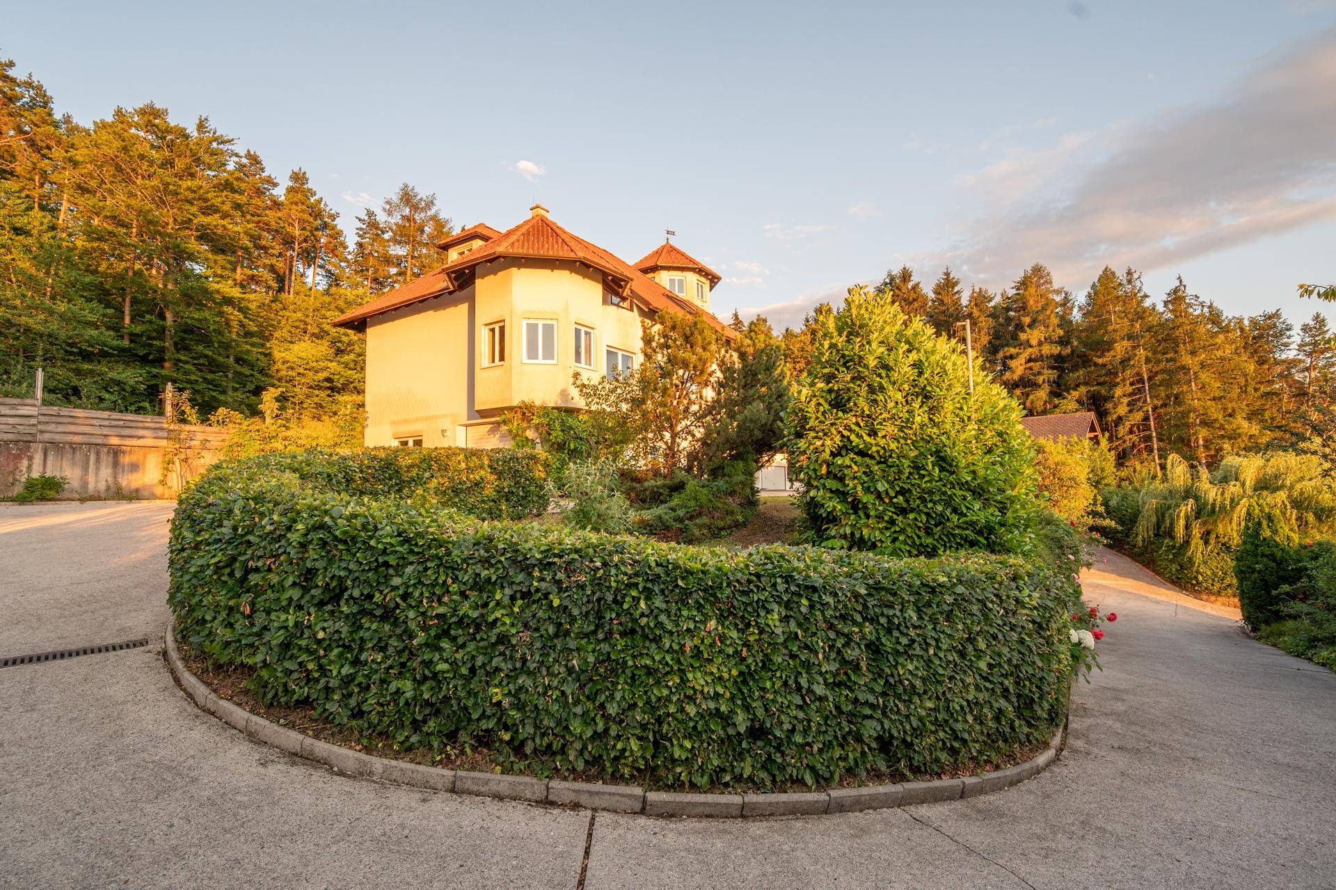 Hausfassade im Abendlicht mit einer gepflegten runden Hecke im Vordergrund.
