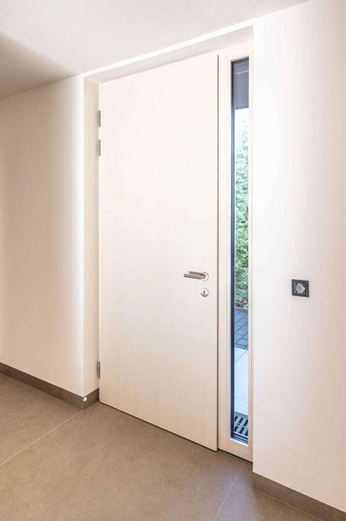 Heller Flur mit moderner weißer Tür und schmalem Seitenfenster für natürliches Licht.