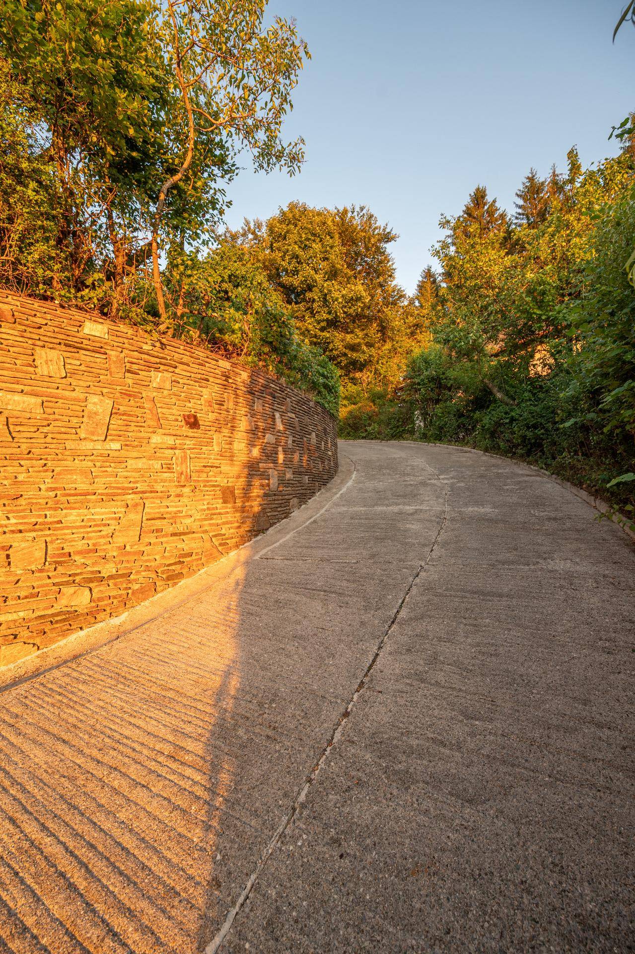 Geschwungene Zufahrt mit einer langen Natursteinmauer im warmen Abendlicht.