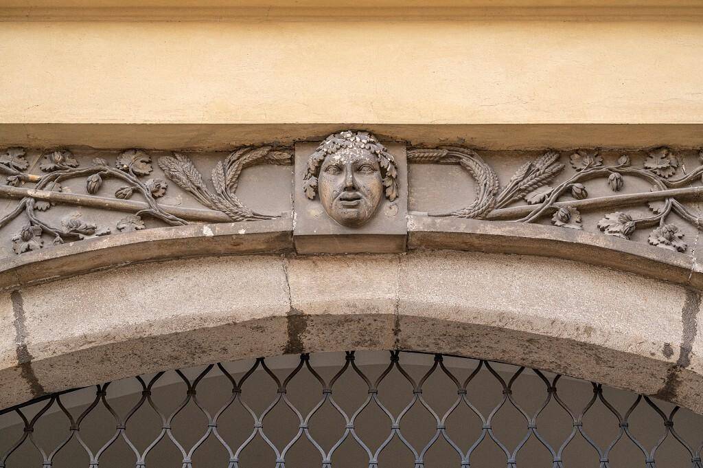 Historische Fassadenverzierung über einem Torbogen mit kunstvollen Details und einem Kopfrelief.