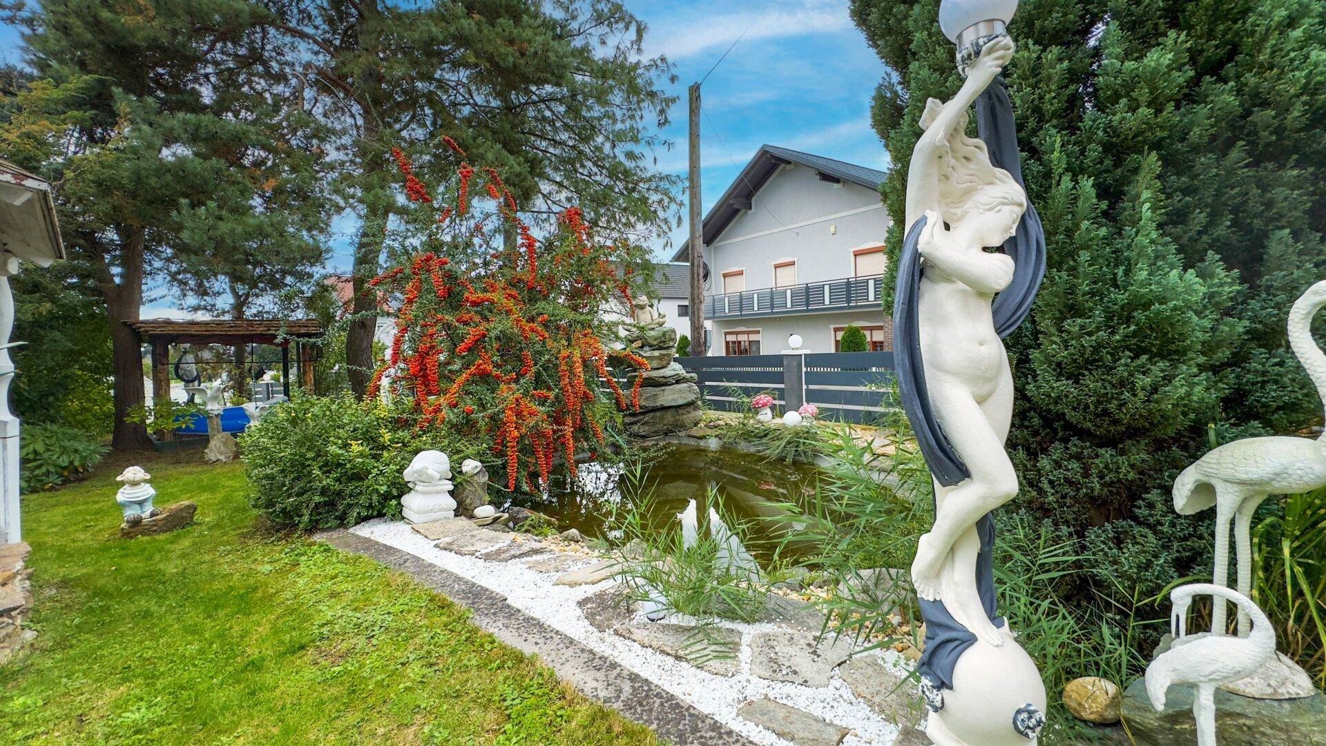 Gepflegter Garten mit einem kleinen Teich, dekorativen Statuen und üppiger Bepflanzung.