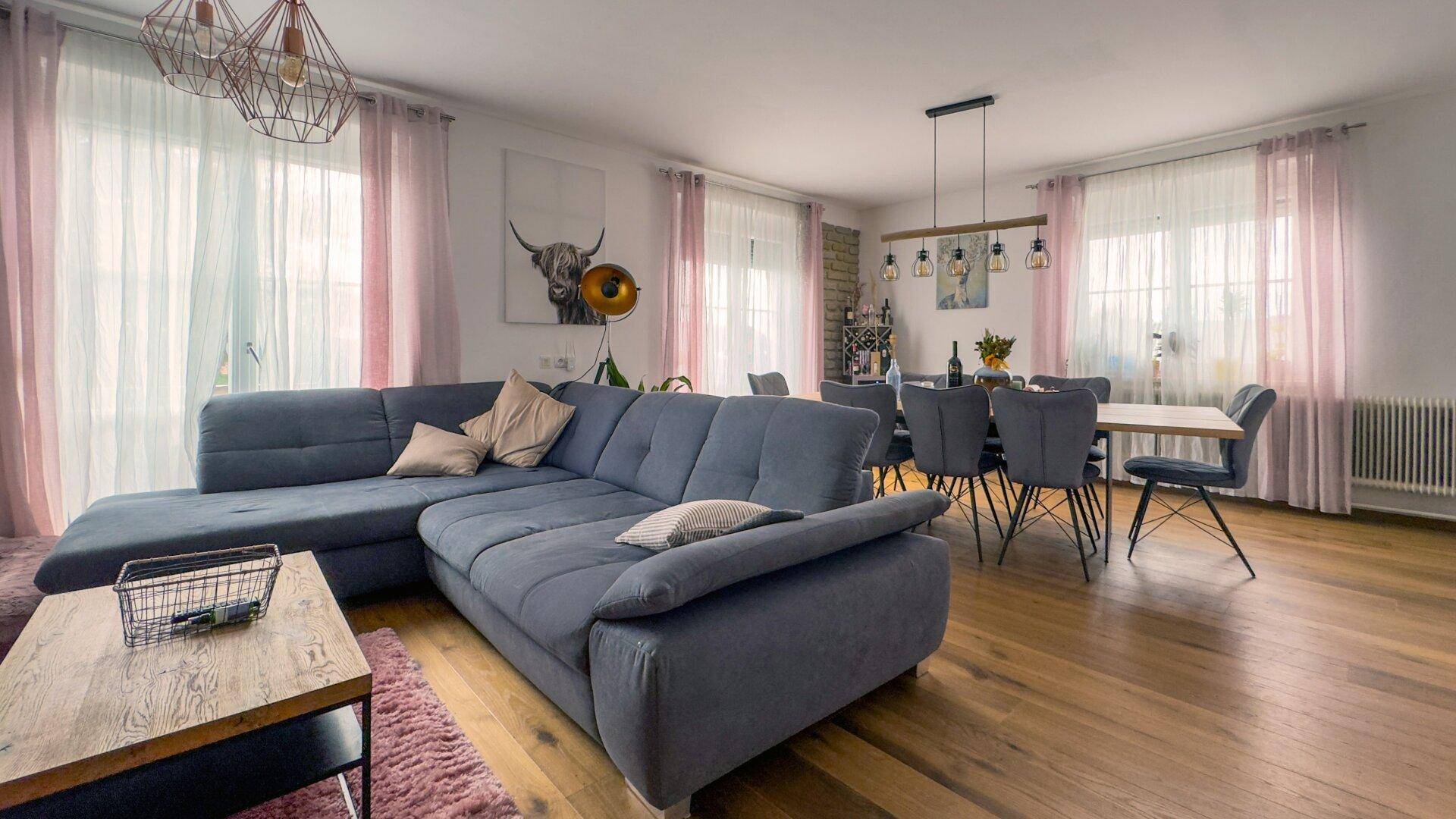Heller, offener Wohn-Essbereich mit Holzboden, großem Sofa und Esstisch.