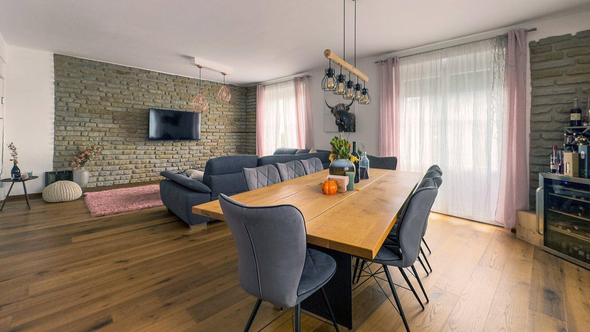 Geräumiger Wohn-Essbereich mit Holzboden, Steinwand und modernem Esstisch für viele Gäste.