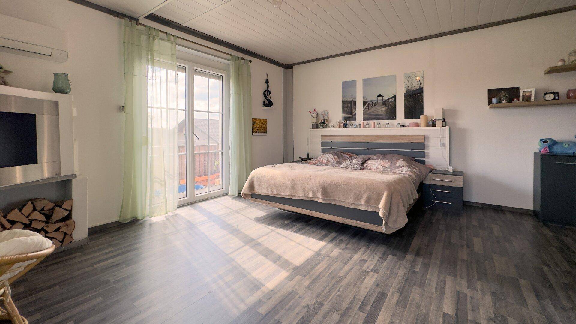 Modernes Schlafzimmer mit dunklem Laminatboden, Doppelbett und Zugang zum Balkon.