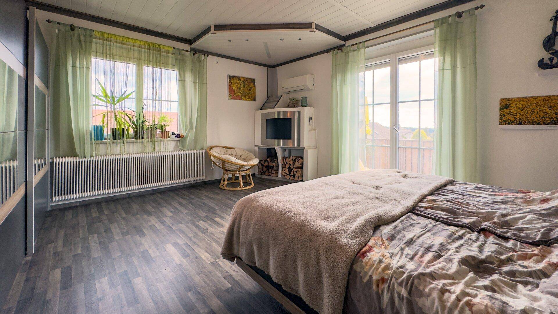 Helles Schlafzimmer mit Laminatboden, Klimaanlage und Fenster mit Blick ins Grüne.