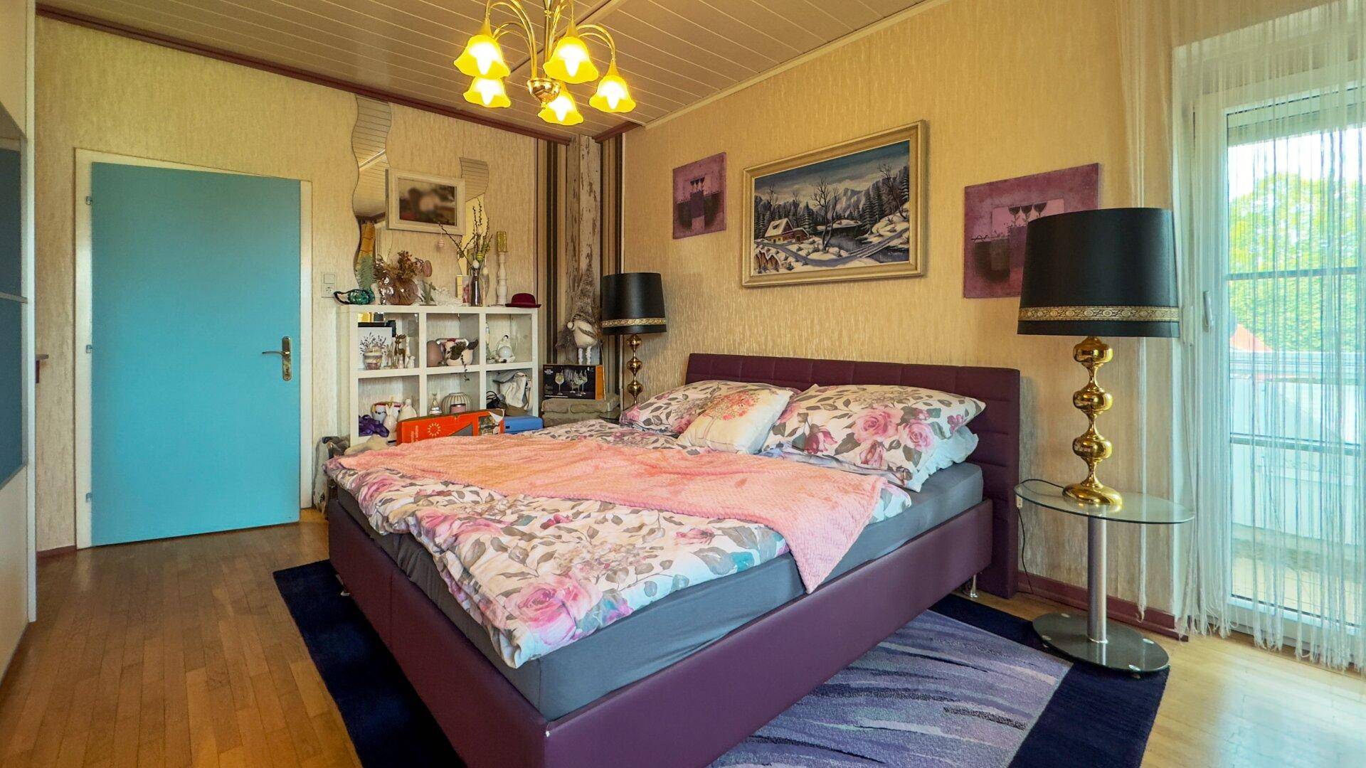 Schlafzimmer mit Holzboden, Doppelbett und Zugang zu einem Balkon oder einer Terrasse.