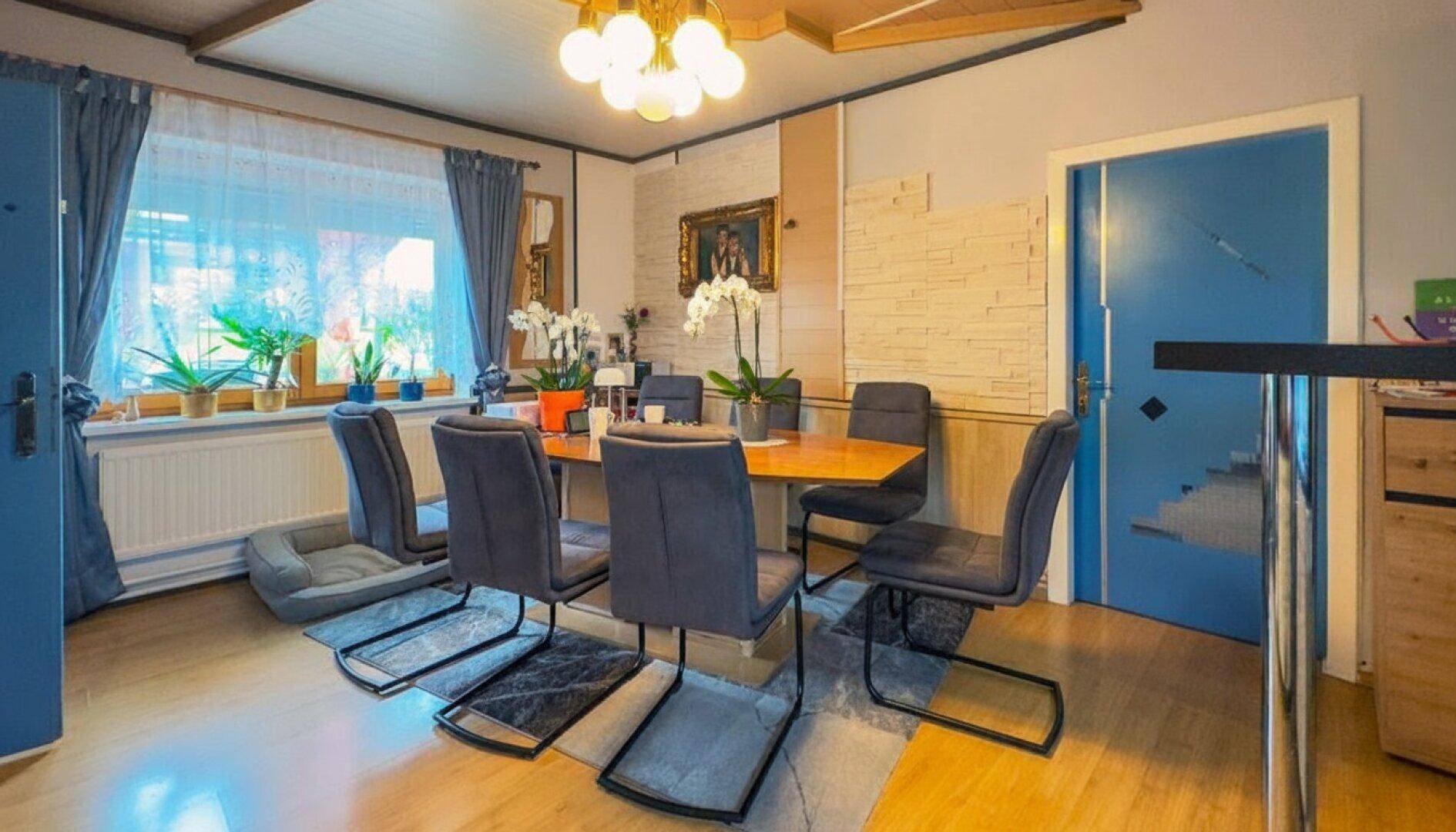 Esszimmer mit Holzboden, großem Esstisch und blauen Türen als Farbakzent.