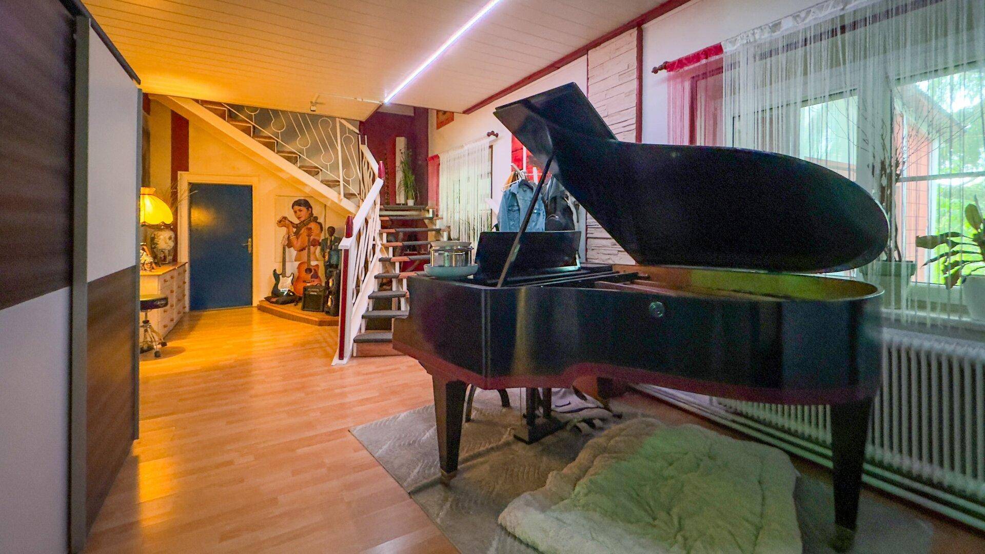 Geräumiger Eingangsbereich mit einem Flügel, einer geschwungenen Treppe und einer Sammlung von Musikinstrumenten.