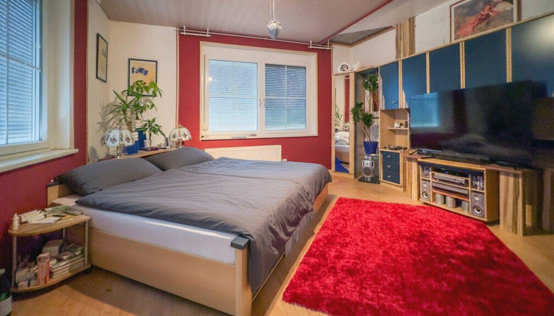 Schlafzimmer mit einem Doppelbett, einem Fernsehschrank und auffälligen roten Wänden.