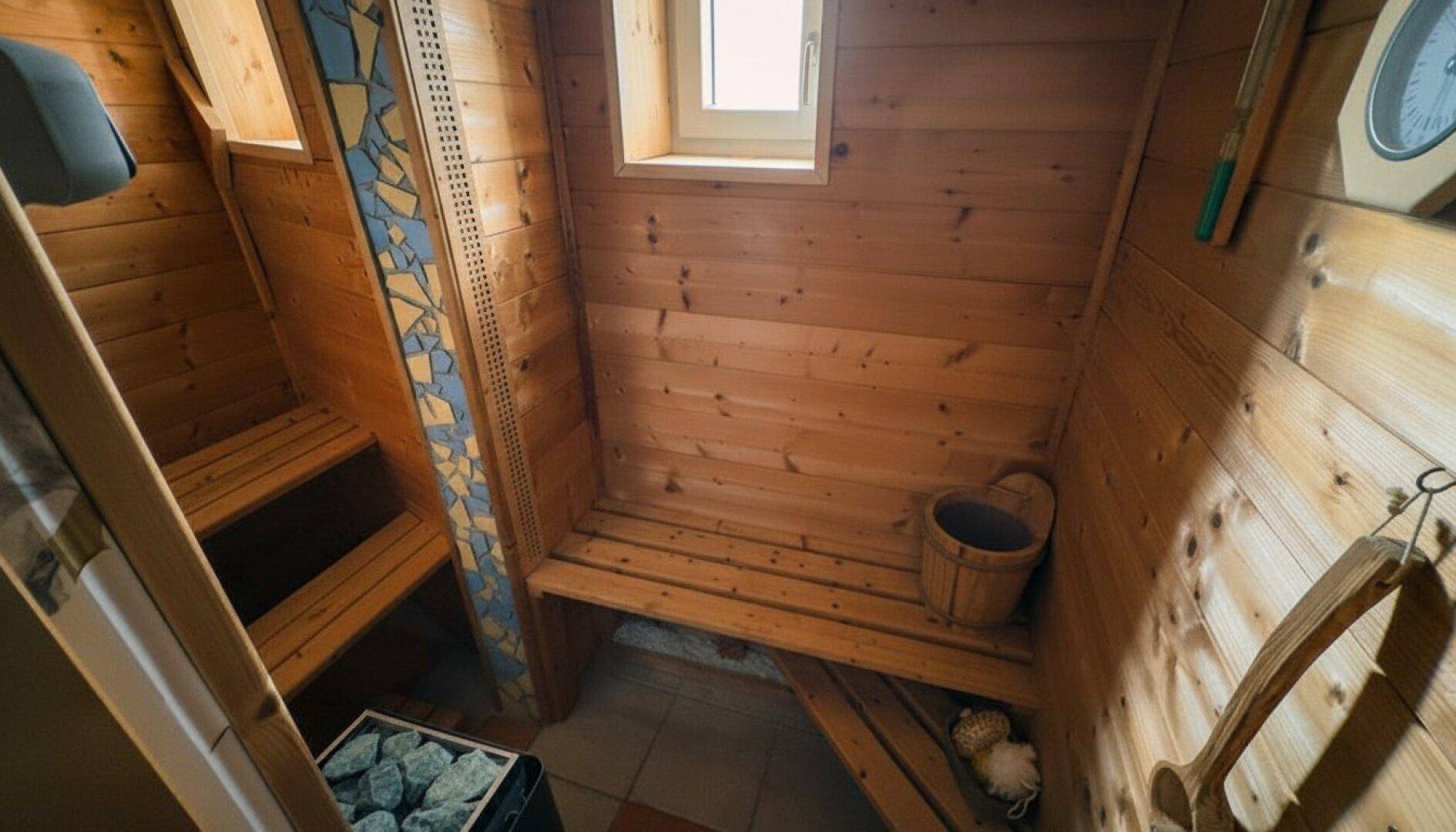 Traditionelle Holzsauna mit Bänken, einem Saunaofen und einem kleinen Fenster.
