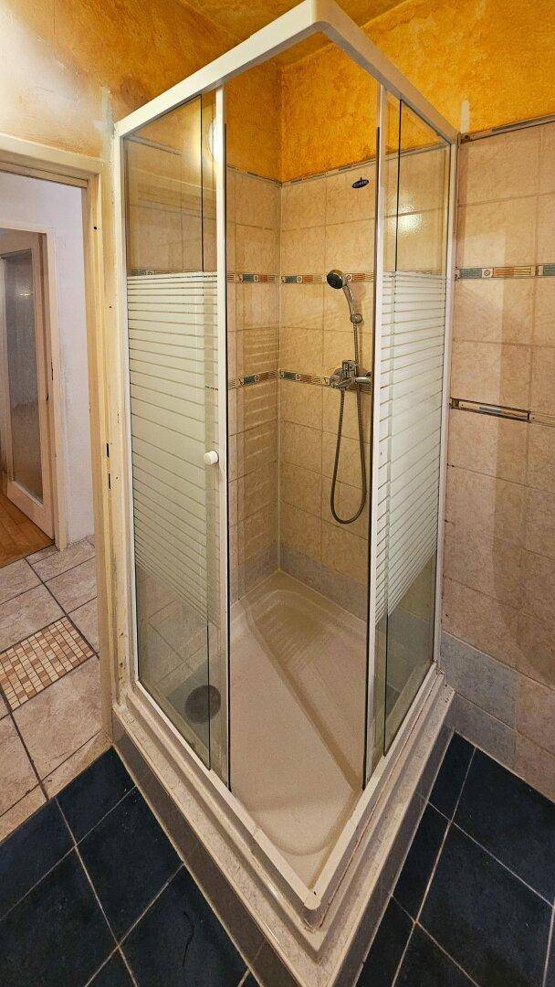 Badezimmer mit Duschkabine, gefliesten Wänden und dunklem Boden.