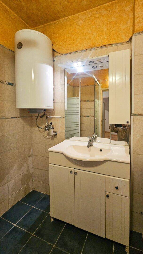 Badezimmer mit Waschbecken, Spiegelschrank und Warmwasserboiler.