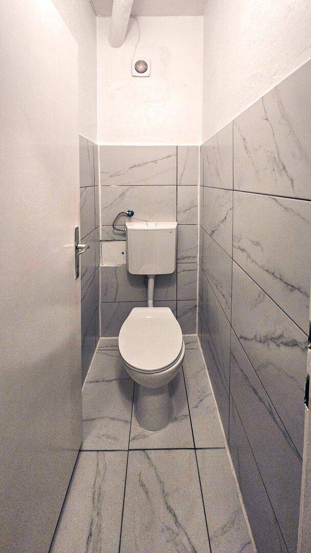 Separate Toilette mit modernen Marmorfliesen an Wänden und Boden.