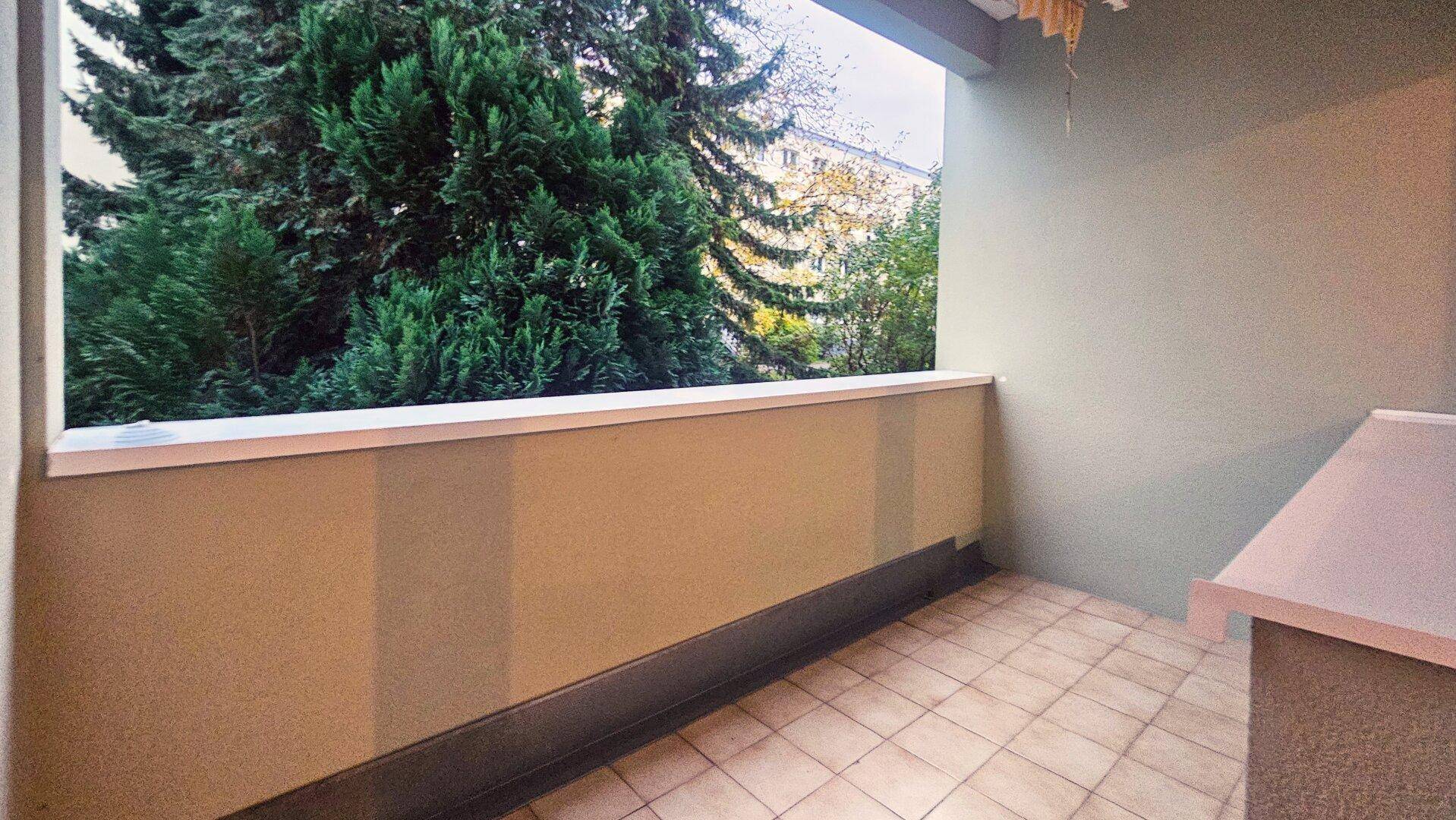 Gefliester Balkon mit Blick ins Grüne und umgebenden Bäumen.