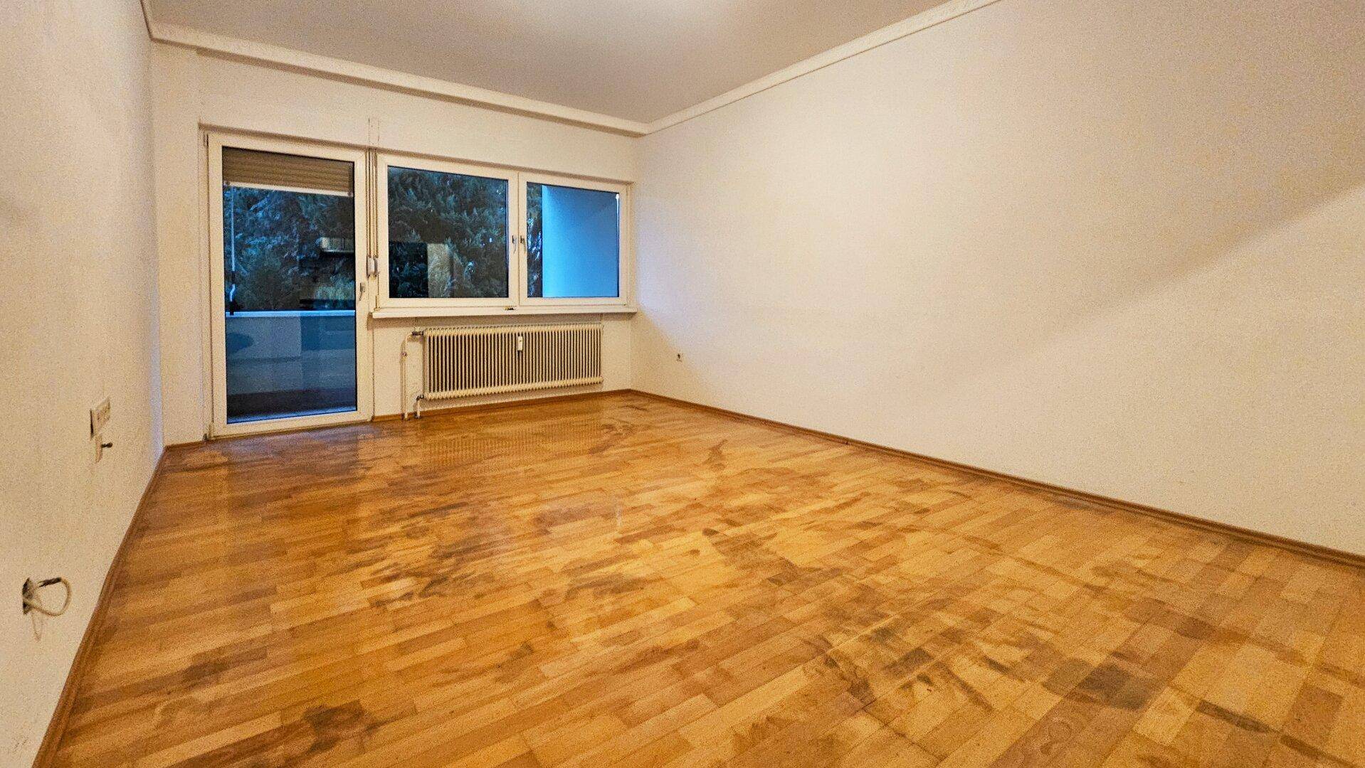 Heller Wohnraum mit Parkettboden und Zugang zu einem Balkon durch große Fenster.