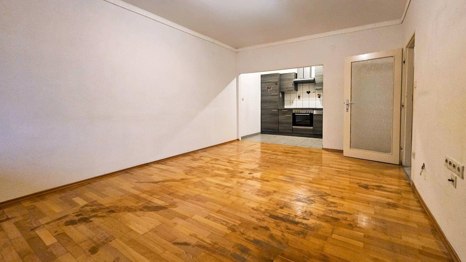 Geräumiger Wohnbereich mit Parkettboden und Durchgang zur modernen Küche.