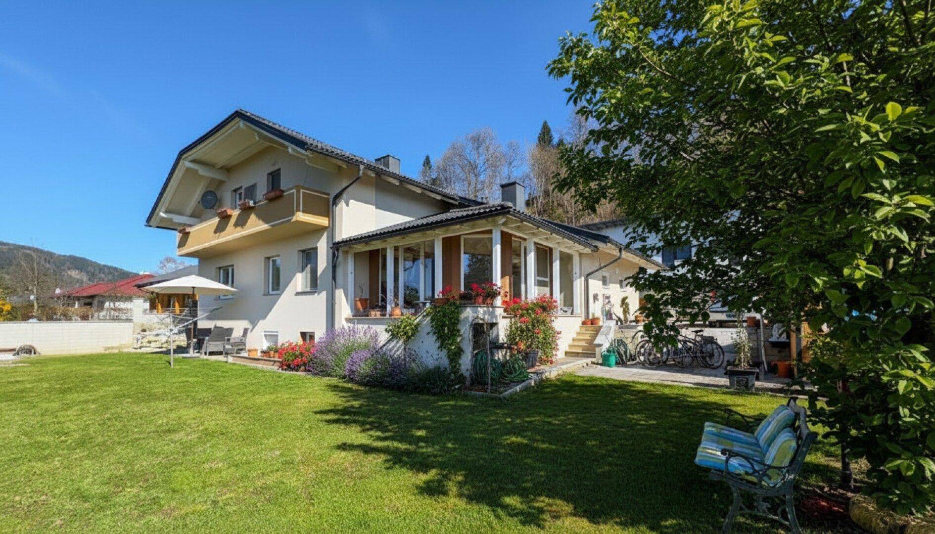 Großzügiger Gartenbereich mit Rasenfläche, Sitzbank und einem Wintergarten am Haus.