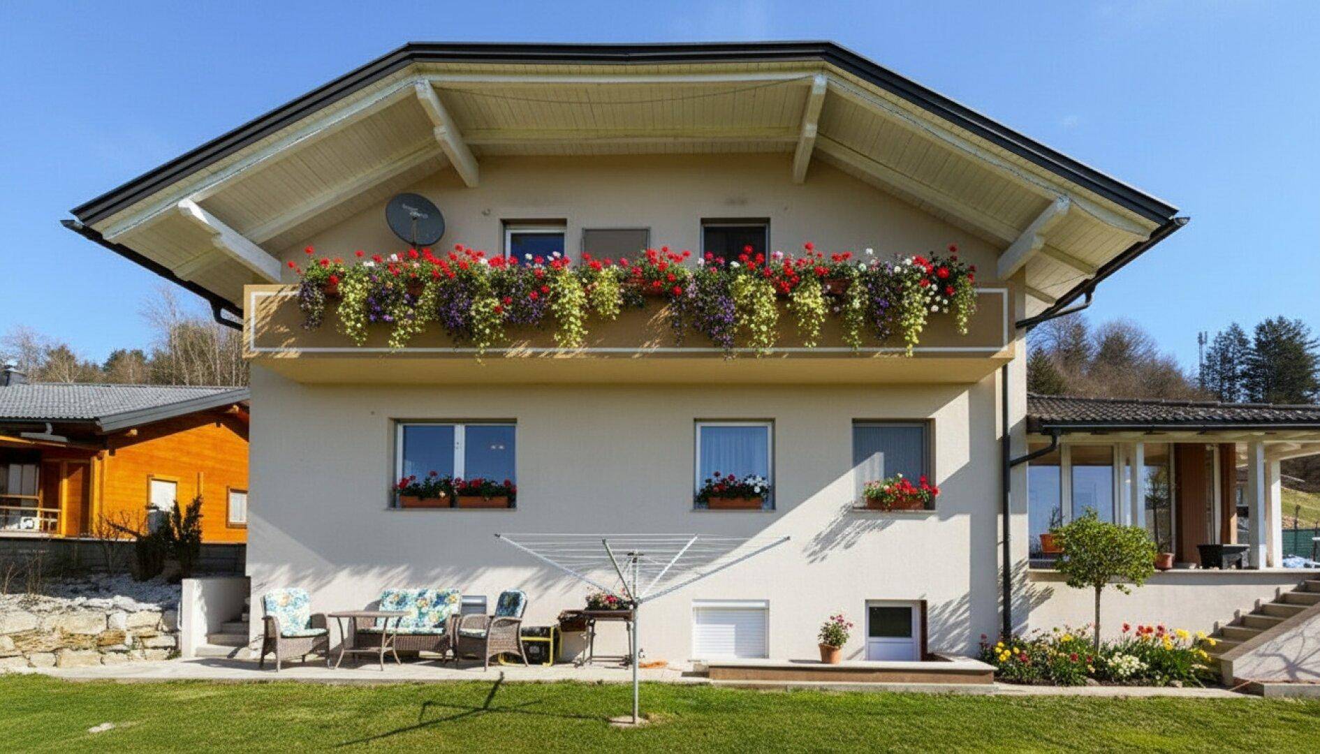 Hausfassade mit blühendem Balkon, Wäscheständer und einer kleinen Terrasse im Garten.