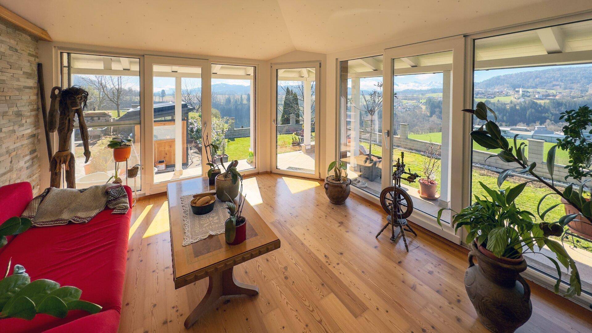 Heller Wintergarten mit Holzboden, großen Fenstern und weitem Blick ins Grüne.