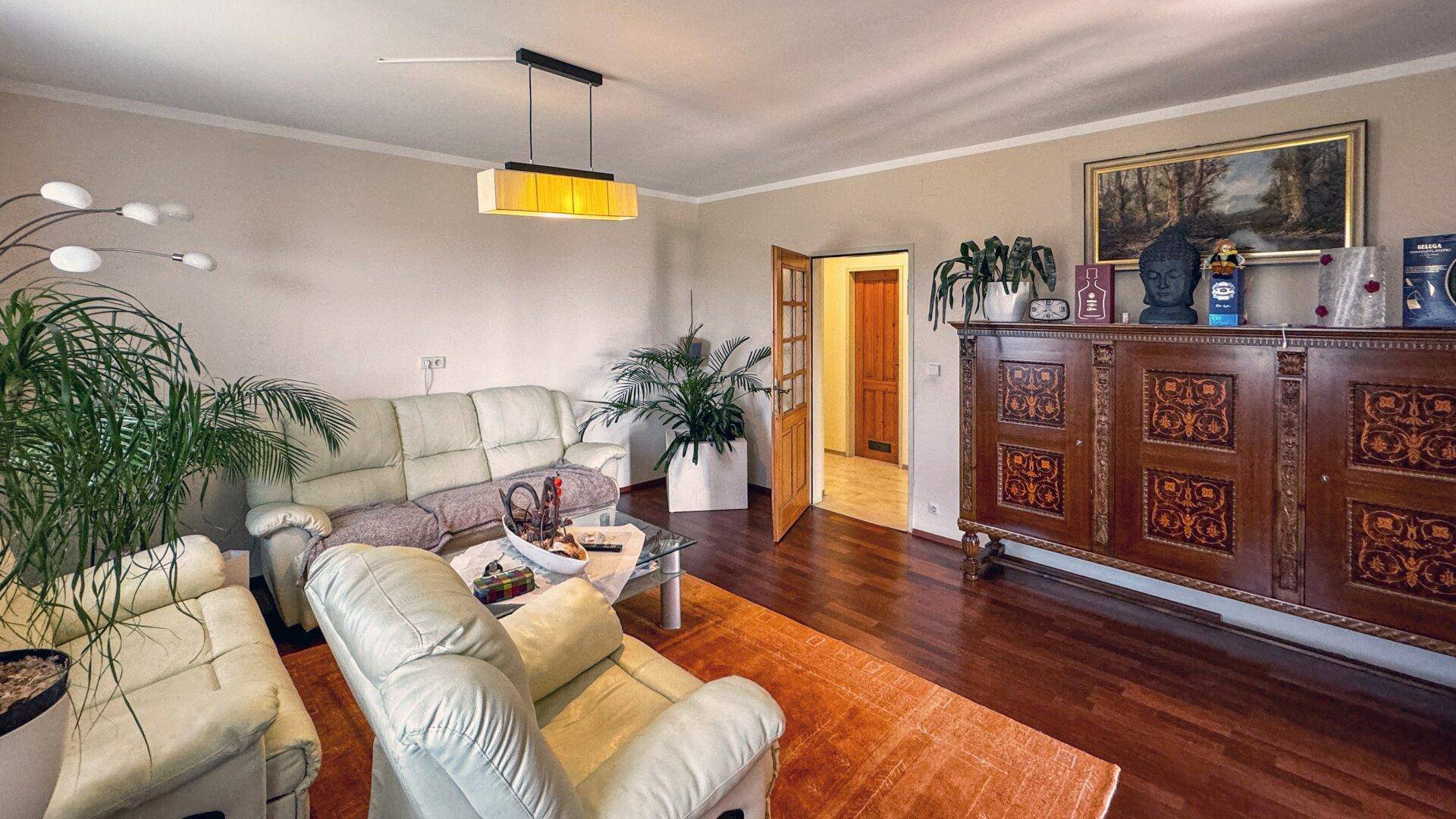 Geräumiges Wohnzimmer mit dunklem Holzboden, traditionellen Möbeln und Blick in den Flur.