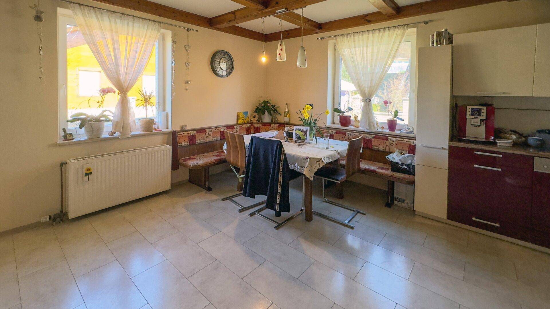 Helle Wohnküche mit Fliesenboden, Holzbalkendecke und gemütlicher Essecke am Fenster.