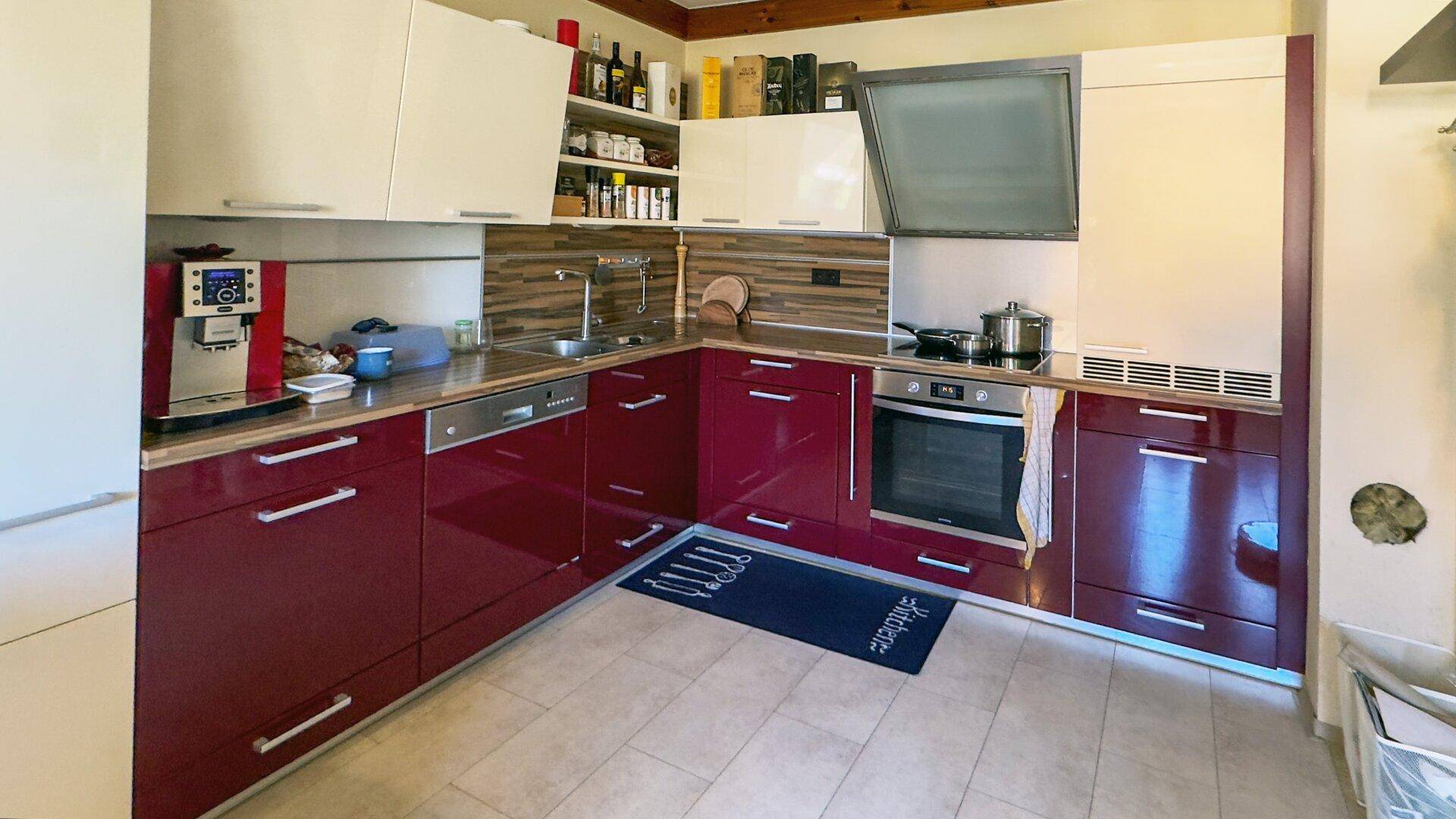 Moderne Einbauküche mit weinroten Hochglanzfronten, Holz-Arbeitsplatte und integrierten Geräten.